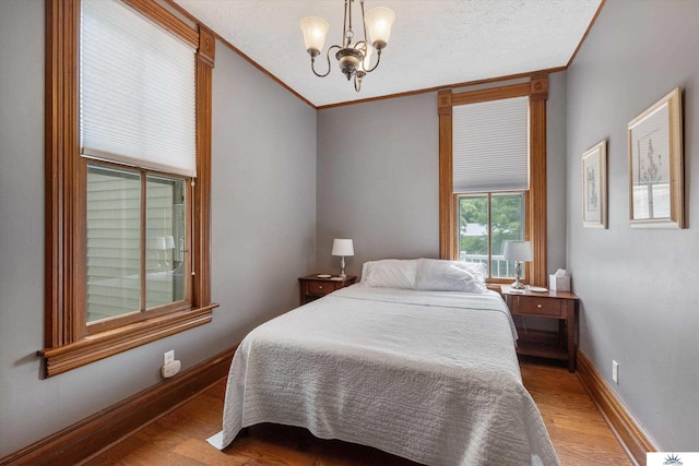 bedroom featuring wood-type flooring, a textured ceiling, crown molding, and an inviting chandelier