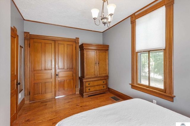 bedroom with light hardwood / wood-style floors, an inviting chandelier, a textured ceiling, and crown molding