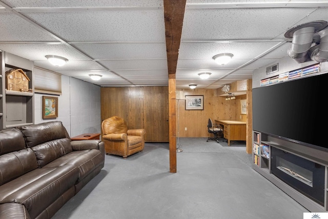 living room featuring wood walls, a drop ceiling, and concrete floors