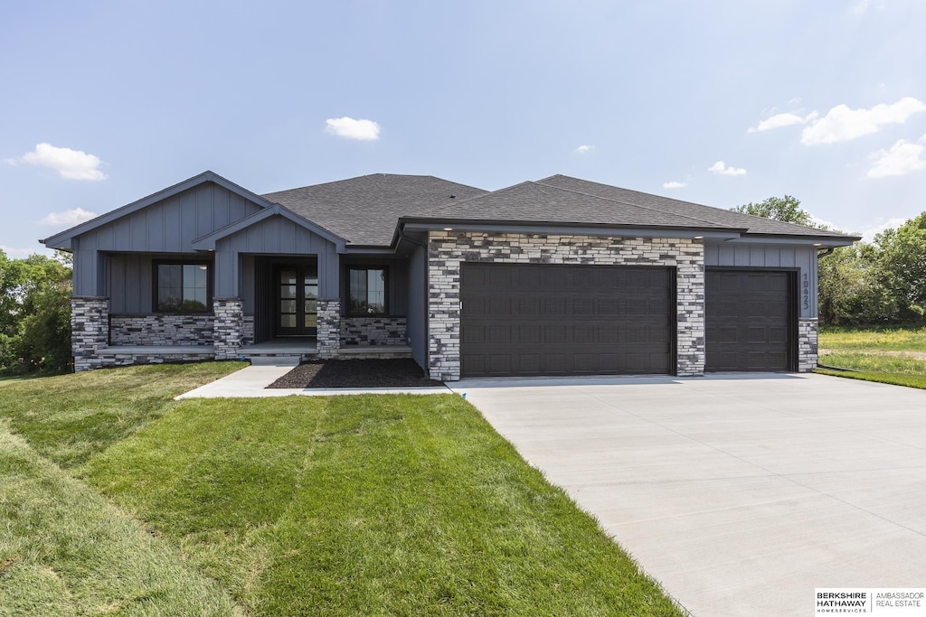 view of front of house featuring an attached garage, a shingled roof, driveway, a front lawn, and board and batten siding