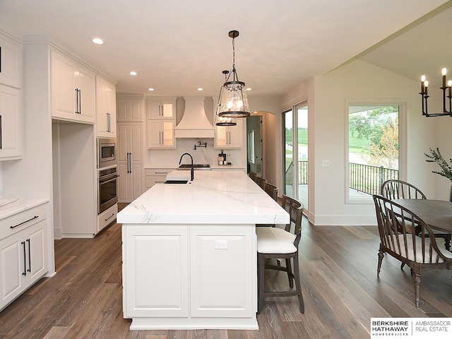 kitchen featuring tasteful backsplash, custom exhaust hood, light stone counters, dark wood-type flooring, and stainless steel appliances