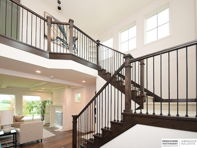 stairway with dark wood-type flooring, a healthy amount of sunlight, and a towering ceiling