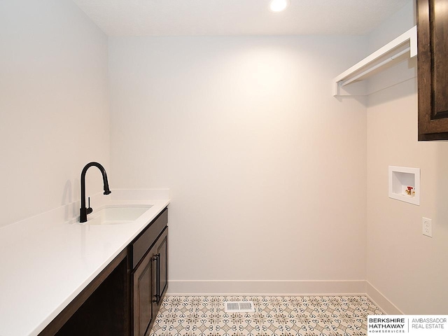 clothes washing area featuring cabinets, sink, light tile patterned floors, and washer hookup