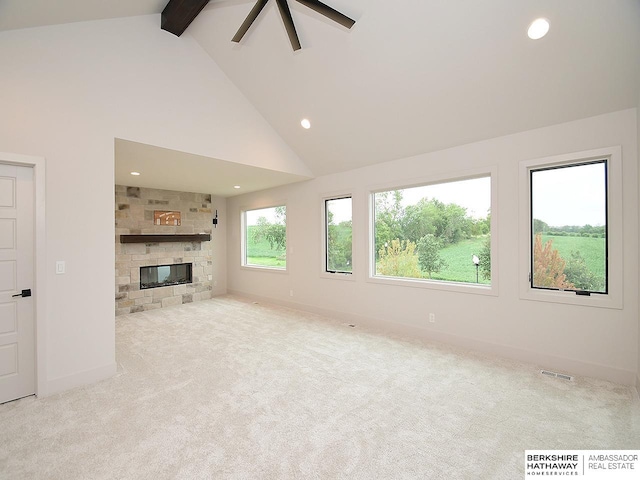 unfurnished living room featuring light carpet, high vaulted ceiling, a stone fireplace, and beam ceiling