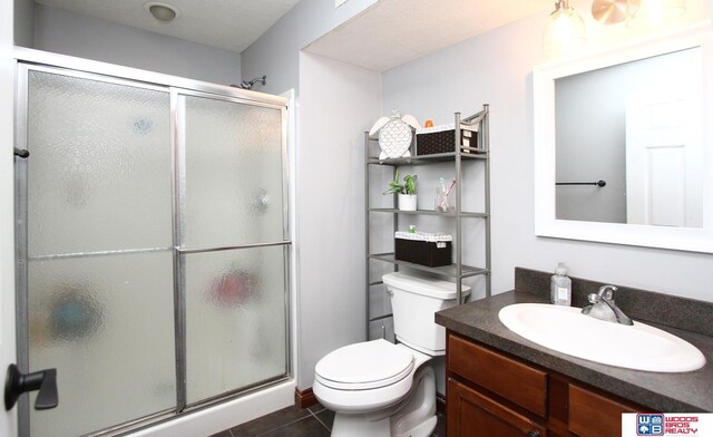 bathroom with a shower with shower door, vanity, tile patterned flooring, and toilet