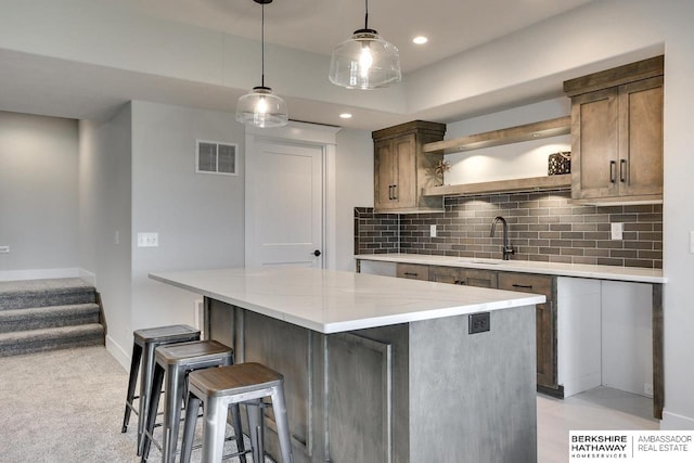 kitchen with decorative light fixtures, sink, decorative backsplash, a center island, and light stone countertops