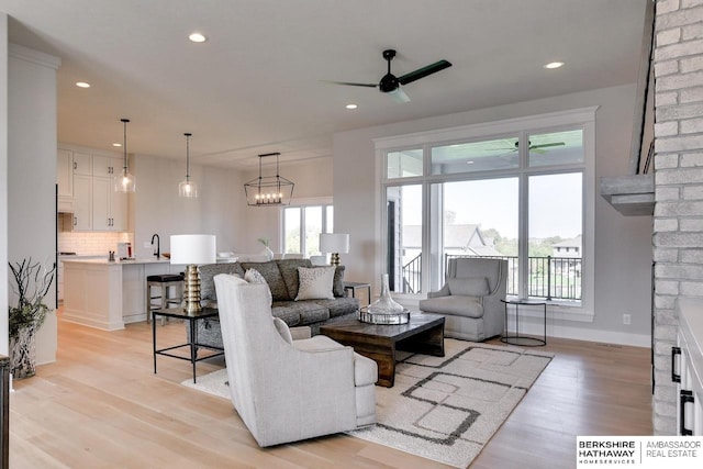 living area featuring ceiling fan with notable chandelier, a fireplace, and light wood-style flooring