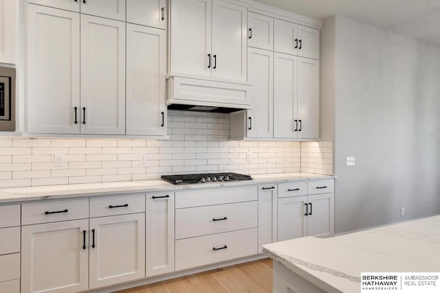 kitchen with tasteful backsplash, white cabinetry, custom exhaust hood, light stone counters, and stainless steel appliances