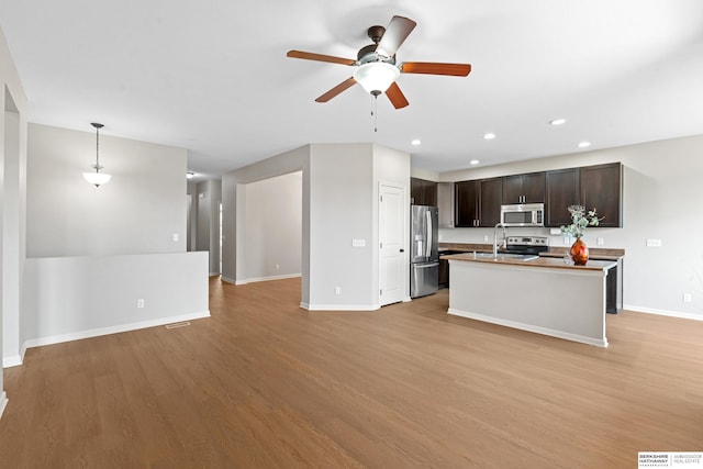 kitchen with appliances with stainless steel finishes, dark brown cabinetry, light wood-type flooring, an island with sink, and ceiling fan