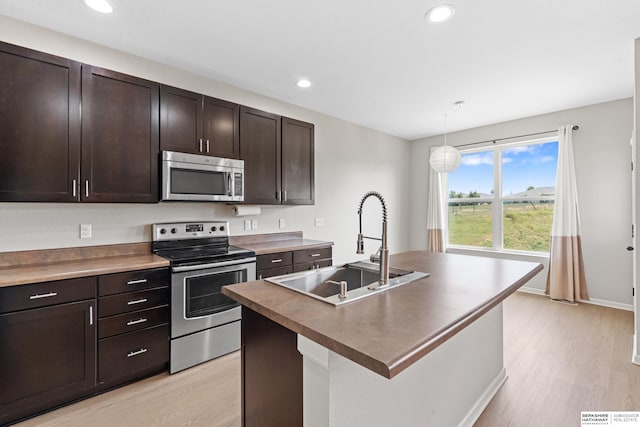 kitchen with stainless steel appliances, light hardwood / wood-style floors, a kitchen island with sink, and sink