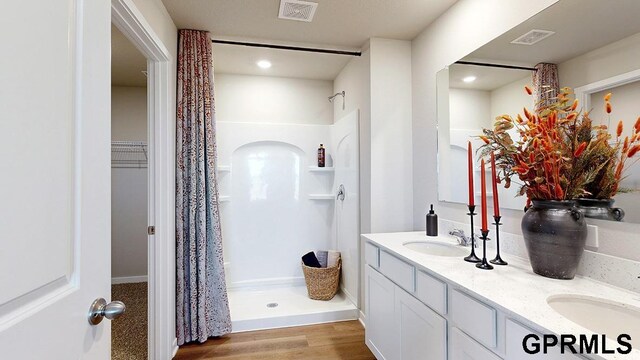 bathroom with dual vanity, a shower, and hardwood / wood-style floors