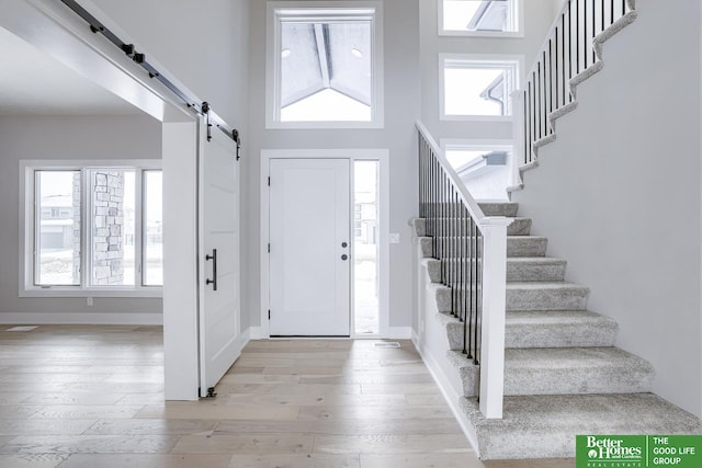 entryway featuring light hardwood / wood-style flooring, a barn door, a wealth of natural light, and a towering ceiling