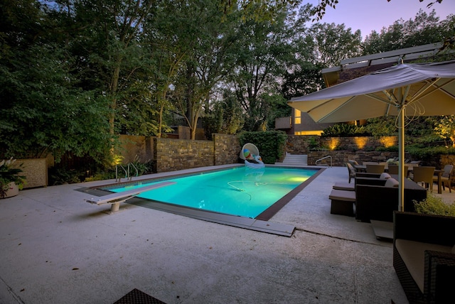 pool at dusk with a diving board and a patio area