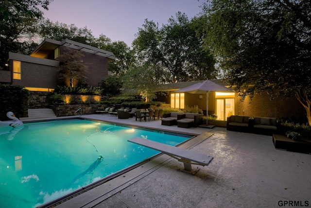 pool at dusk featuring a patio, an outdoor hangout area, and a diving board