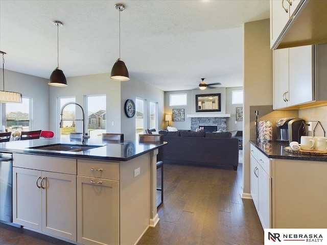 kitchen featuring a sink, a ceiling fan, dark wood-style floors, a fireplace, and pendant lighting