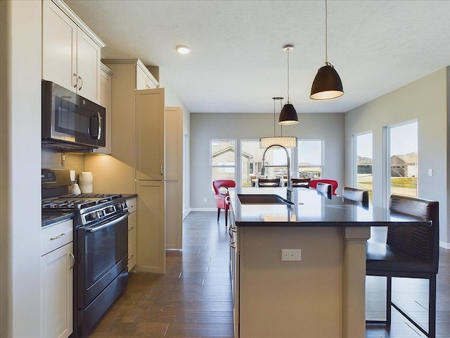 kitchen featuring black microwave, a breakfast bar, gas stove, dark countertops, and a sink