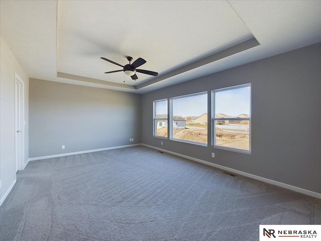 unfurnished room with a tray ceiling, baseboards, and visible vents