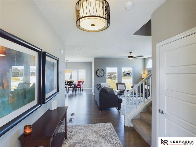 living room with a textured ceiling, ceiling fan, and dark wood-type flooring