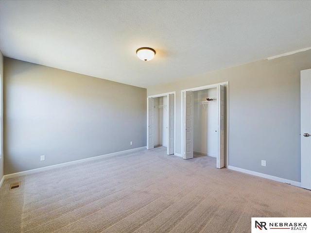 unfurnished bedroom featuring two closets, a textured ceiling, light colored carpet, visible vents, and baseboards