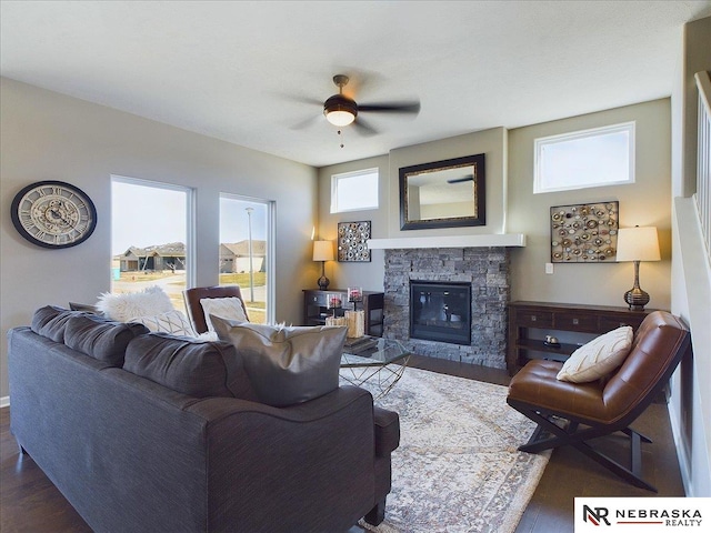 living room with a stone fireplace, dark wood-type flooring, and ceiling fan