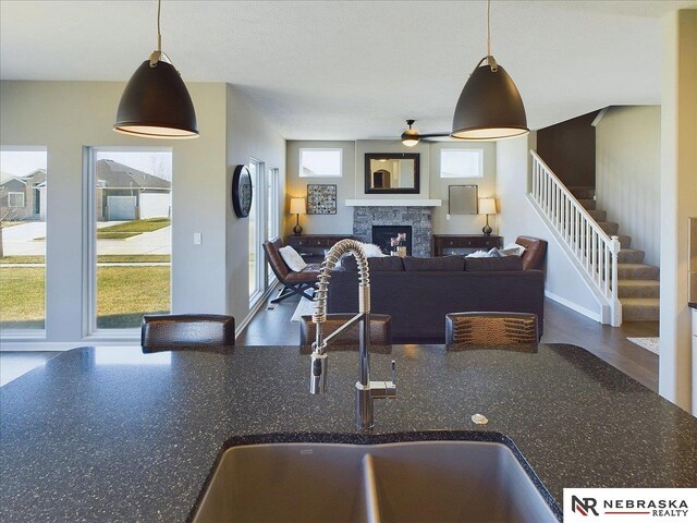 kitchen with ceiling fan, a sink, a stone fireplace, and hanging light fixtures