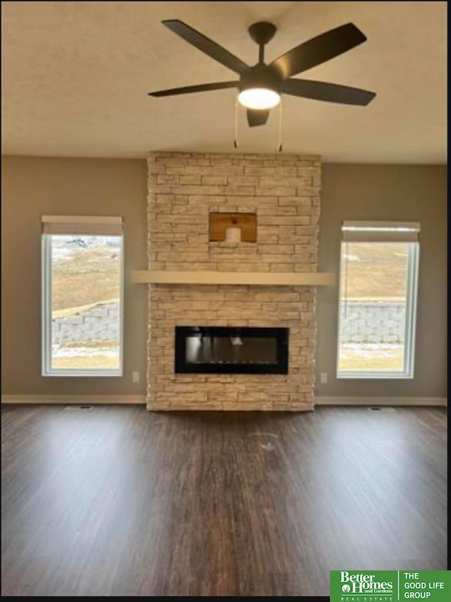 unfurnished living room featuring a stone fireplace, plenty of natural light, dark wood-type flooring, and ceiling fan