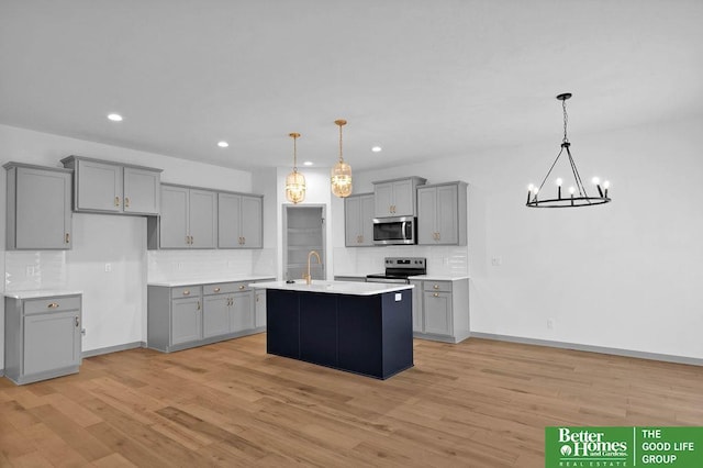 kitchen featuring light countertops, stainless steel appliances, light wood finished floors, gray cabinetry, and backsplash