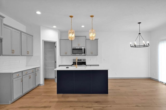 kitchen with tasteful backsplash, an inviting chandelier, light wood finished floors, gray cabinetry, and stainless steel appliances