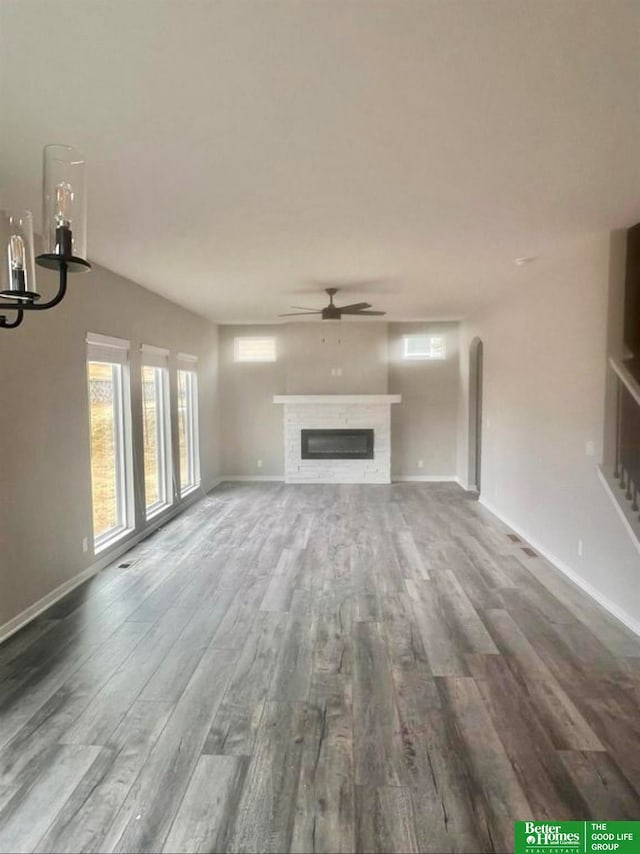 unfurnished living room with ceiling fan with notable chandelier and wood-type flooring