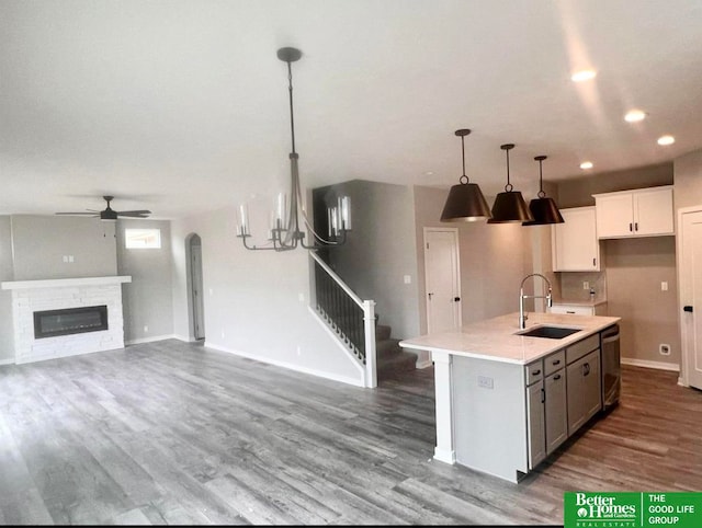 kitchen with a stone fireplace, sink, white cabinetry, decorative light fixtures, and a center island with sink