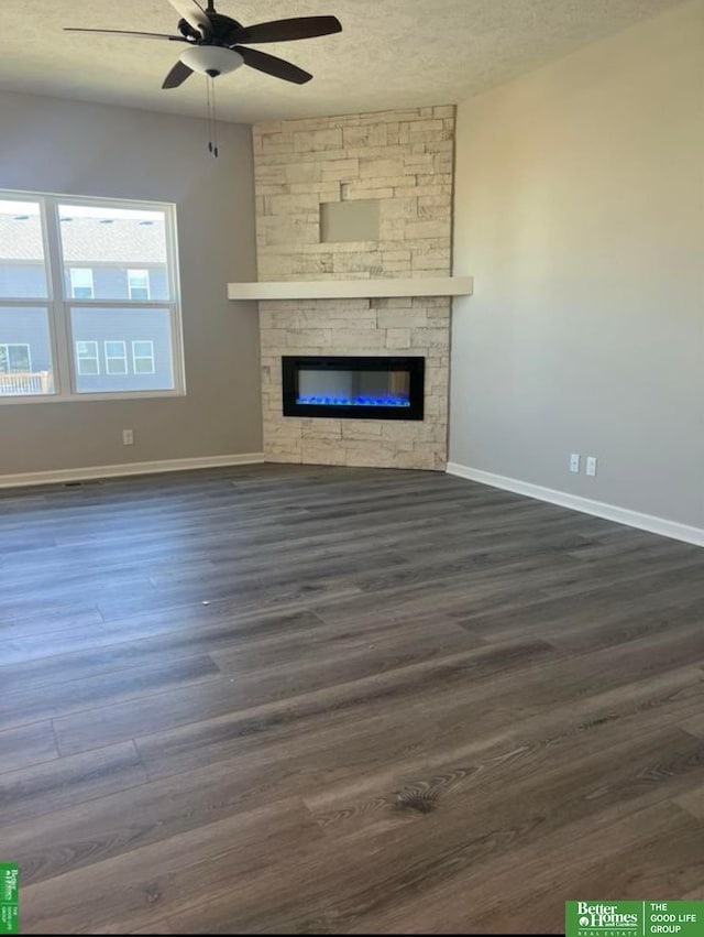 unfurnished living room featuring a textured ceiling, ceiling fan, a stone fireplace, and dark hardwood / wood-style flooring