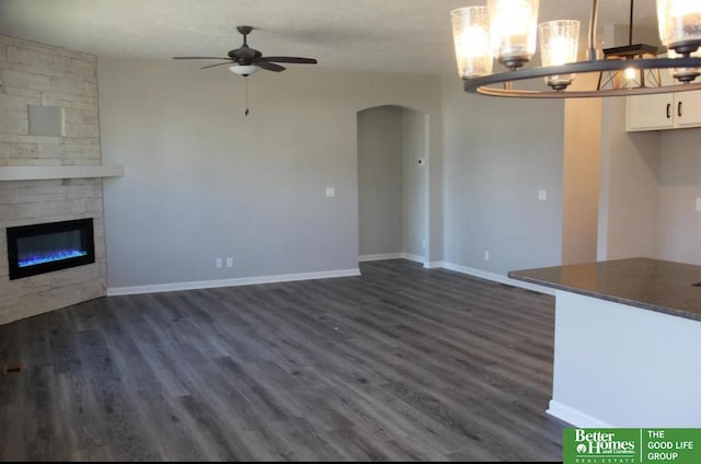 unfurnished living room featuring ceiling fan with notable chandelier, dark hardwood / wood-style flooring, a textured ceiling, and a stone fireplace