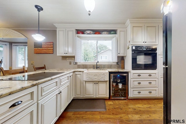 kitchen with black appliances, wine cooler, sink, and light hardwood / wood-style floors