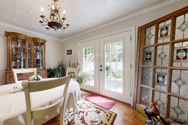 dining area with french doors, hardwood / wood-style flooring, ornamental molding, and an inviting chandelier