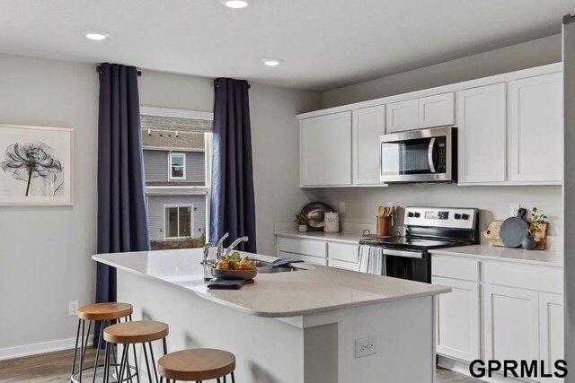 kitchen featuring white cabinetry, an island with sink, stainless steel appliances, sink, and wood-type flooring