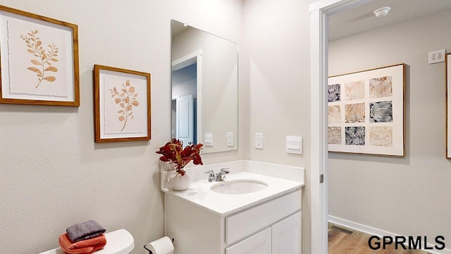 bathroom with toilet, vanity, and wood-type flooring