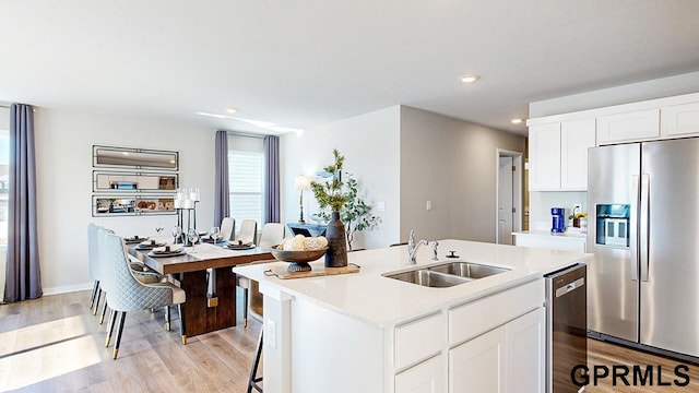 kitchen with light hardwood / wood-style flooring, white cabinetry, appliances with stainless steel finishes, a center island with sink, and sink