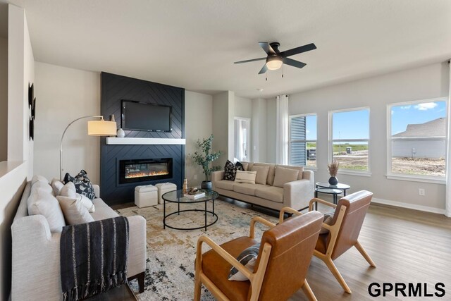 living room featuring ceiling fan, a large fireplace, and light hardwood / wood-style floors