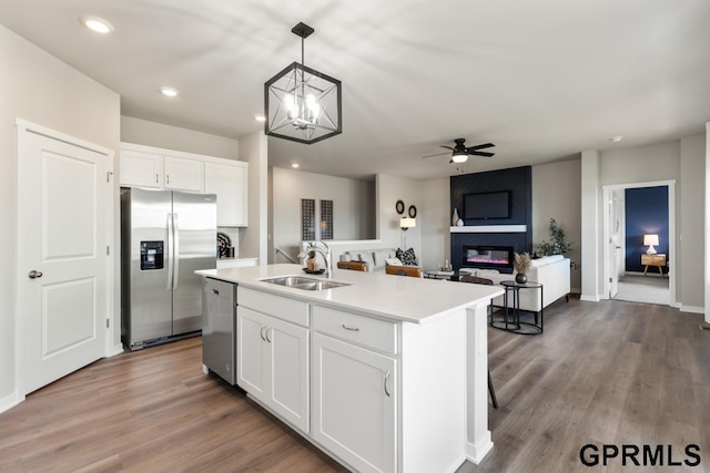 kitchen with appliances with stainless steel finishes, an island with sink, decorative light fixtures, sink, and white cabinetry