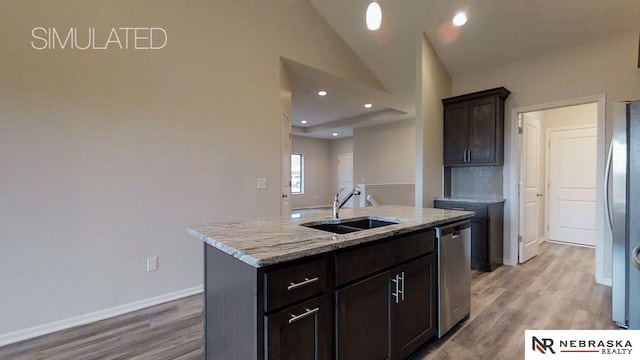 kitchen with vaulted ceiling, appliances with stainless steel finishes, an island with sink, sink, and light stone countertops