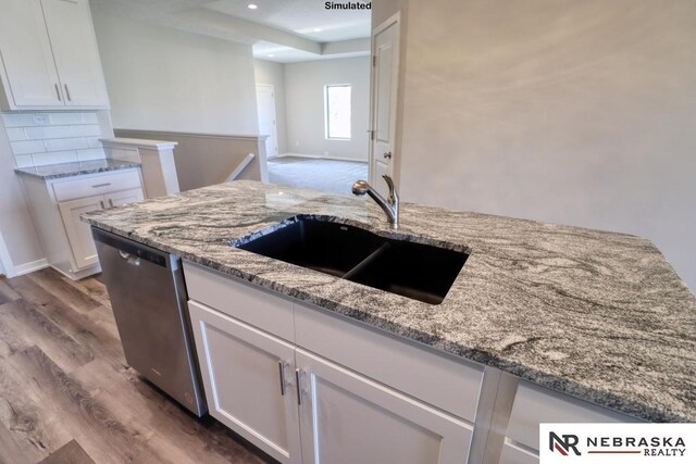 kitchen with light stone counters, white cabinetry, dishwasher, and sink