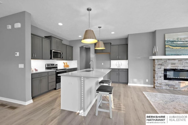 kitchen with decorative light fixtures, gray cabinets, a center island with sink, and appliances with stainless steel finishes