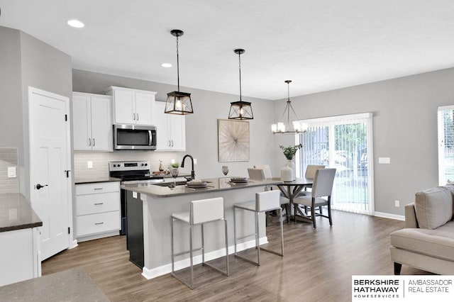 kitchen with stainless steel appliances, decorative light fixtures, a kitchen bar, decorative backsplash, and white cabinets