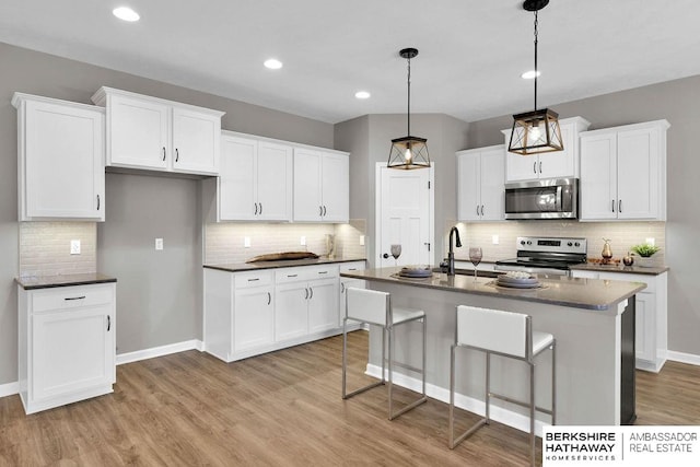 kitchen with appliances with stainless steel finishes, sink, a center island with sink, decorative light fixtures, and white cabinetry