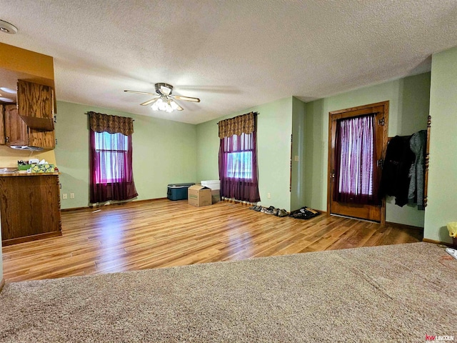 unfurnished living room with ceiling fan, a textured ceiling, and light hardwood / wood-style floors