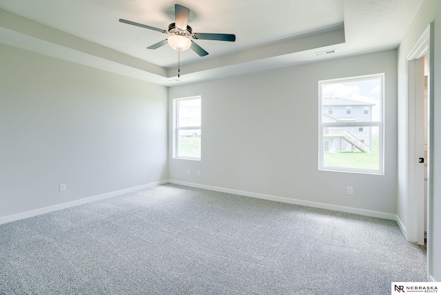 unfurnished room with ceiling fan, a tray ceiling, and carpet