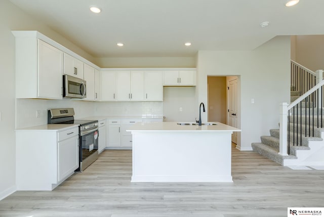 kitchen featuring decorative backsplash, white cabinetry, appliances with stainless steel finishes, a center island with sink, and light wood-type flooring