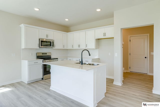 kitchen with light wood-type flooring, appliances with stainless steel finishes, a kitchen island with sink, backsplash, and sink