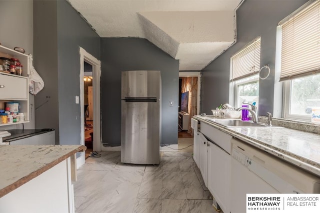 kitchen featuring white dishwasher, white cabinets, stainless steel refrigerator, light tile patterned floors, and sink