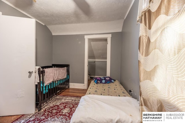 bedroom with ceiling fan, a textured ceiling, vaulted ceiling, and hardwood / wood-style flooring